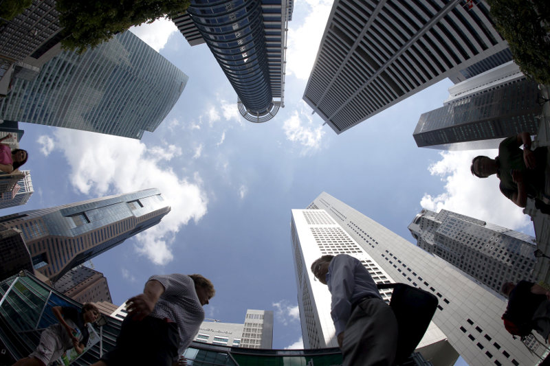 People walk past office buildings at the central business district in Singapore April 14, 2015. Singapore's central bank on Tuesday surprised markets by holding them off from further monetary easing, 