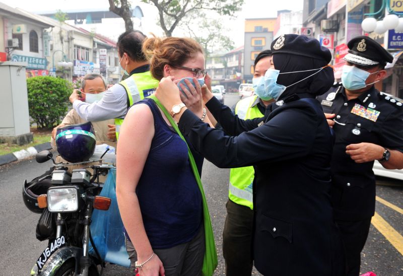 A policewoman helps a tourist put on a mask in Kuching, Sarawak, September 23, 2015. The air pollutant index in Kuching was an unhealthy 127 yesterday. u00e2u20acu2022 Bernama pic