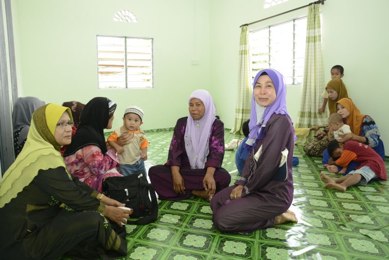 Happy recipient, Puan Ruzaini (second right in foreground) invites her neighbours for a gathering at her new home in Galas, Gua Musang.