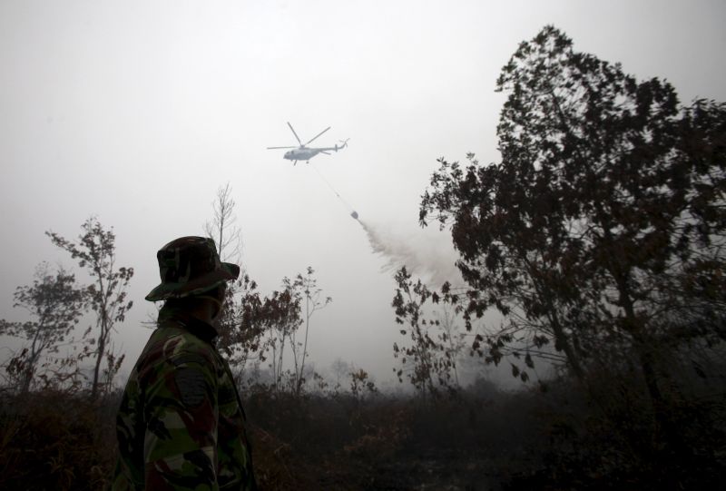 An Indonesian soldier watches as a helicopter water bomber releases its cargo over a peatland fire in Kampar, Riau province on the Indonesian island of Sumatra, September 17, 2015. u00e2u20acu2022 Reuters pic