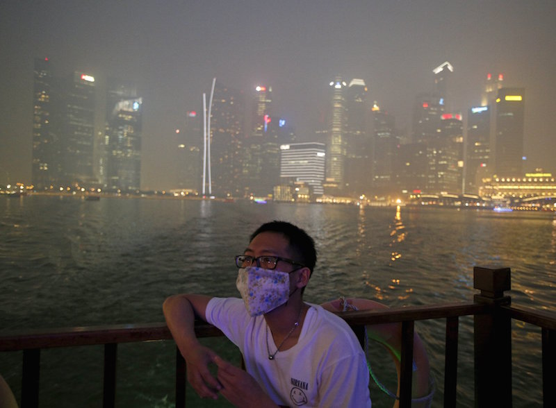 A man wearing a mask watches from a bumboat as he passes the haze-shrouded central business district in Singapore September 24, 2015. u00e2u20acu201d Reuters pic