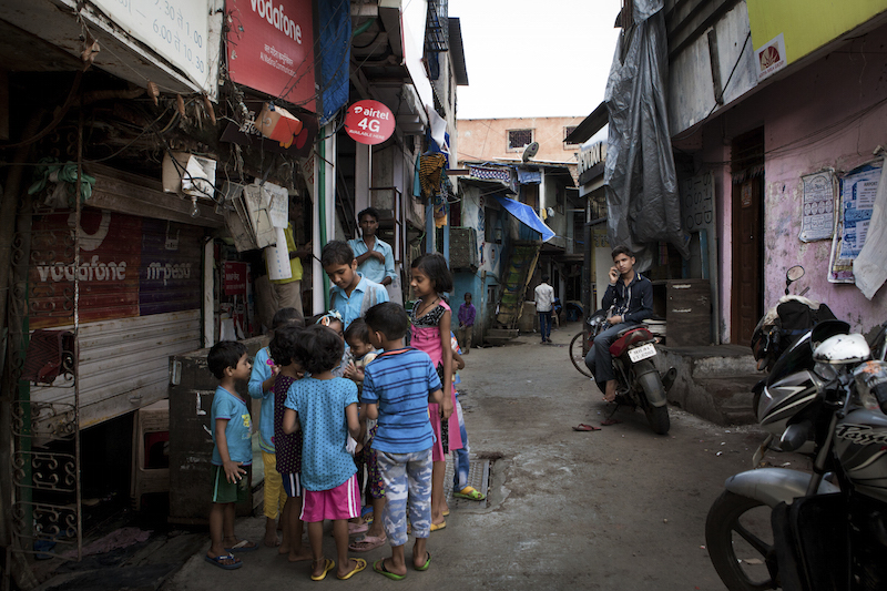 A young man speaks on his cellphone as children play in the streets of Dharavi in Mumbai August 19, 2015. u00e2u20acu201d Picture by Asmita Parelkar/The New York Times