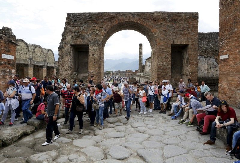 Tourists walk an ancient Roman cobbled street as workers in hard hats beaver away, peering through screens and wire fences at ruins of ancient houses where restorations are going into overdrive.