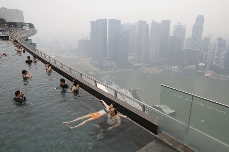 People swim in an infinity pool overlooking the skyline of the central business district shrouded by haze in Singapore September 14, 2015. REUTERS/Edgar Su