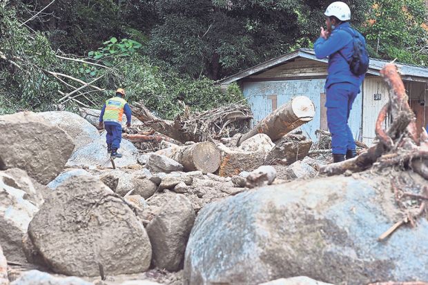 Workers survey an affected area before bringing in machinery to clear the logs and rocks. u00e2u20acu201d Picture by Azinuddin Ghazali