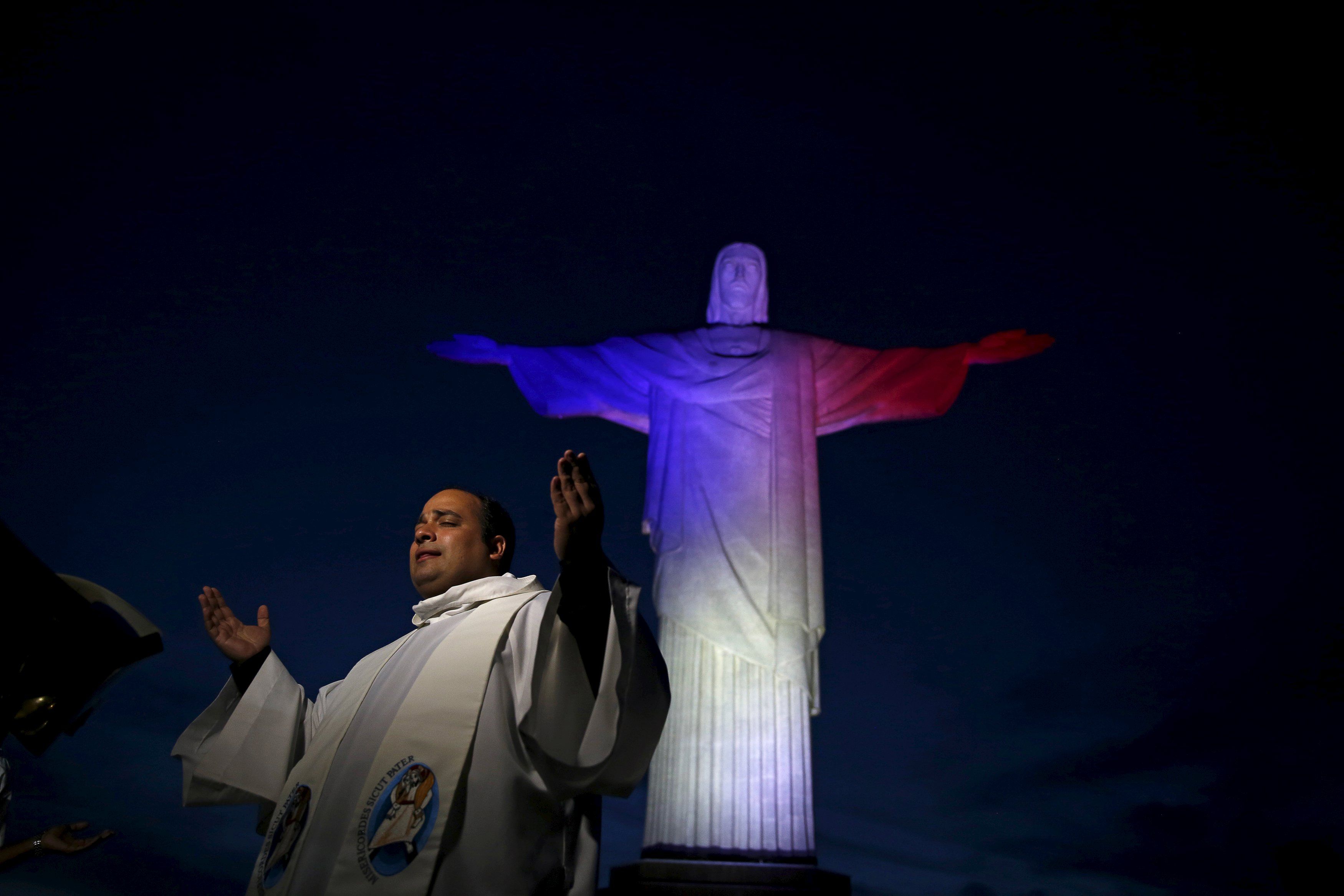 A priest gestures during an event in tribute to the victims of Paris attacks, as the Christ the Redeemer is lit up in France's official colours in Rio de Janeiro, November 14, 2015. u00e2u20acu201d Reuters