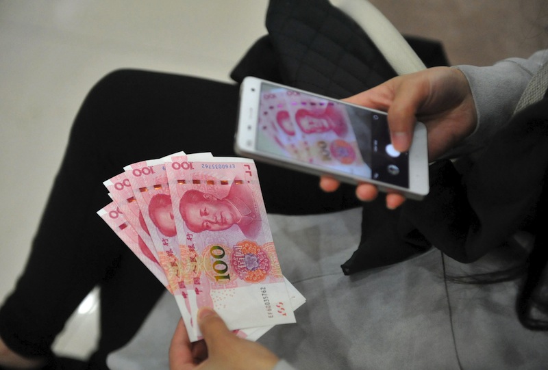 A woman takes pictures of new 100 yuan banknotes she withdrew from a bank in Hangzhou, Zhejiang province, China, November 12, 2015. u00e2u20acu201d Reuters pic