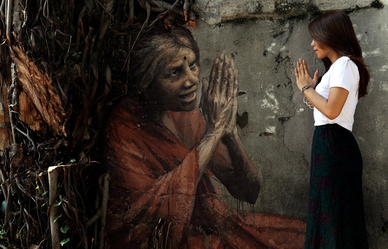 A visitor gestures as she looks at a mural of an elderly Indian lady greeting tourists at Lorong Lumut, George Town, on December 4, 2015. This mural is the third installation done by Russian artist Julia Volchkova in Penang. u00e2u20acu201d Bernama pic