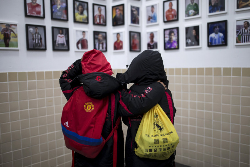 Students carry backpacks with logos of Manchester United Football Club (left) and Royal Madrid Football Club while looking at photos of famous football players at Evergrande football academy in Qingyuan, southern China December 3, 2015.