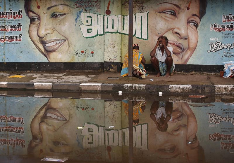 A flood-affected couple December 6, 2015, sits along a flooded roadside under a picture of Jayalalithaa Jayaram.