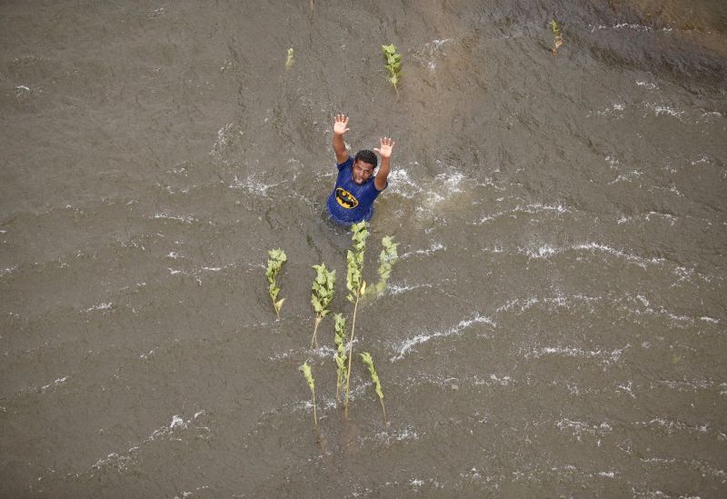 A man stranded in floodwaters tries to catch the attention of an Indian coast guard helicopter for relief supply.