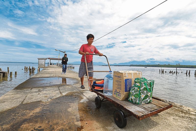 A resident helps a nurse to get her belongings and other necessities to the clinic from the Pulau Pasir Hitam jetty. u00e2u20acu2022 Malay Mail pic