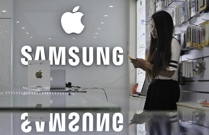 A sales assistant uses her mobile phone next to the company logos of Apple and Samsung at a store in Hefei, Anhui province September 10, 2014. u00e2u20acu201d Reuters pic