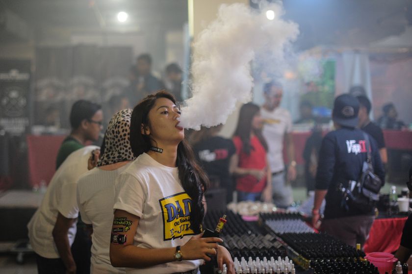 This picture taken on December 5, 2015 shows a promoter (centre) smoking an electronic cigarette during the Vape Fair in Kuala Lumpur. u00e2u20acu2022 AFP picnn