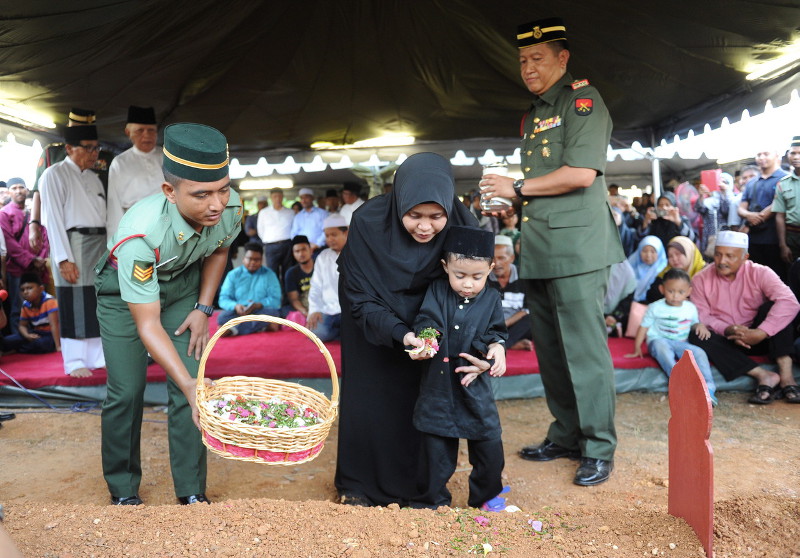 Siti Hazwani Ahmad helping her eldest son Akhil Tahfiz Hasman, 3, to lay a wreath on the grave of her husband, the late Captain Hasman Husin who was buried at the Solok Air Batu cemetery in Masjid Tanah, Malacca on Jan 6, 2016. u00e2u20acu201d Bernama pic