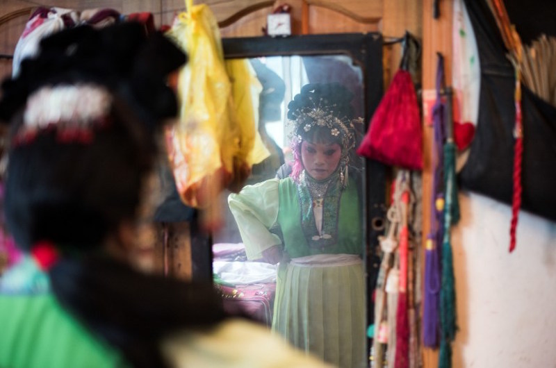 This picture taken on January 7, 2016 in Kunming shows Zhong Huifangi, of the ‘Flower Lantern’ troupe being reflected in a mirror while getting dressed during a show. — AFP pic