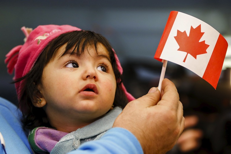 A young Syrian refugee looks up as her father holds her and a Canadian flag at the as they arrive at Pearson Toronto International Airport in Mississauga, Ontario, December 18, 2015. u00e2u20acu201d Reuters pic