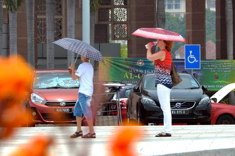 Picture shows a foreign tourist who cannot stand the heat sipping water while holding an umbrella at Dataran Putra Putrajaya, March 20, 2016. u00e2u20acu201d Bernama pic 