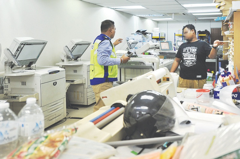 An officer from the Subang Commercial Crime Division questioning a suspect at the printing shop. Scanners, a central processing unit and thumb drives were among the equipment seized. u00e2u20acu201d Malay Mail pic