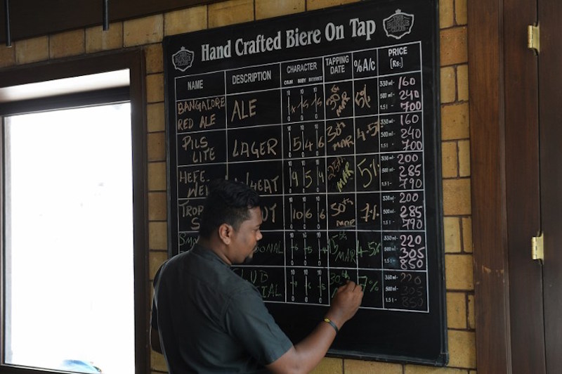 A member of staff writes descriptions of the craft beer made at the microbrewery on a blackboard at The Biere Club in Bangalore March 30, 2016. — AFP pic