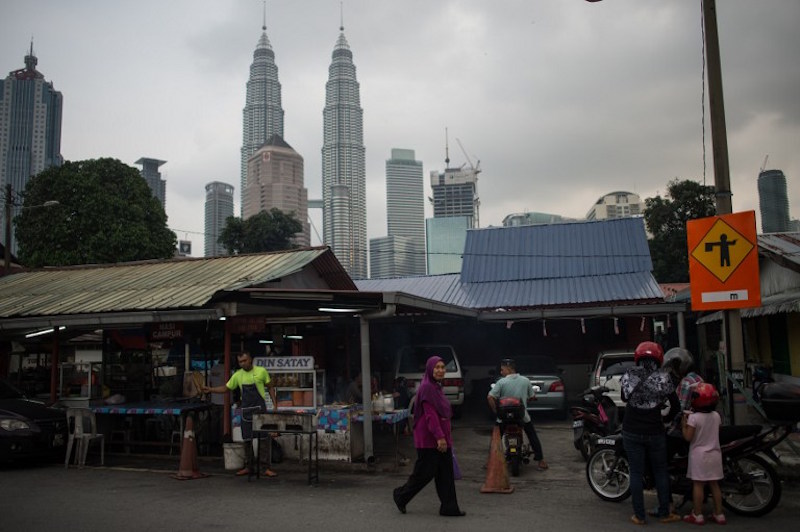 A woman walks past a restaurant as Malaysia’s iconic Petronas Twin Towers loom in the background in Kampung Baru, Kuala Lumpur, March 22, 2016. — AFP pic