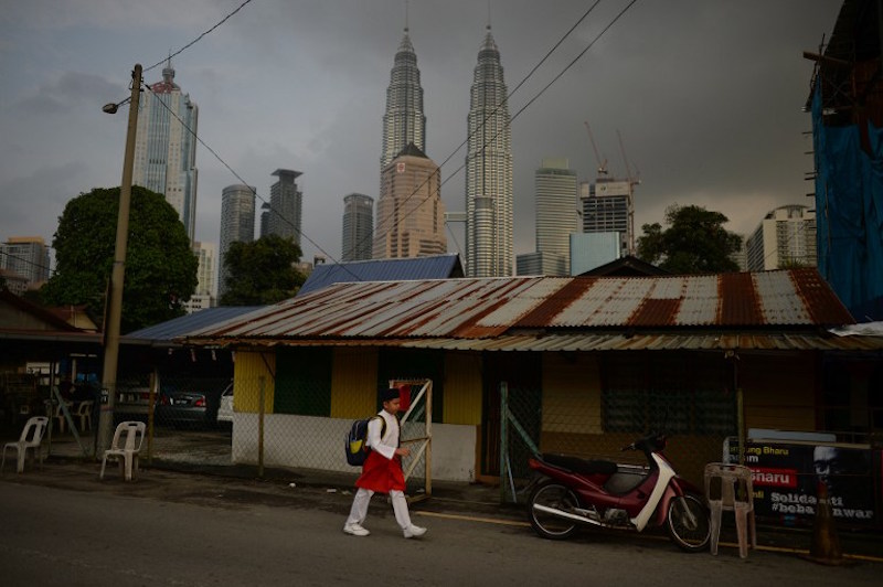 A boy walks past a wooden home as Malaysiau00e2u20acu2122s iconic Petronas Twin Towers loom in the background in Kampung Baru, Kuala Lumpur. u00e2u20acu201d AFP picn