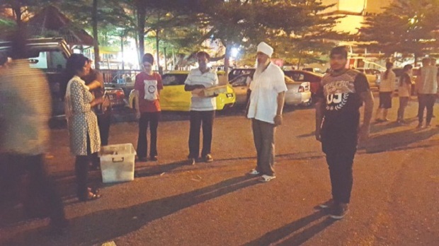 Deep Singh, in his trademark white shirt and turban, chats with his crew during a lull in the hectic feeding programme at the Kota Raya car park. u00e2u20acu201d Malay Mail pic