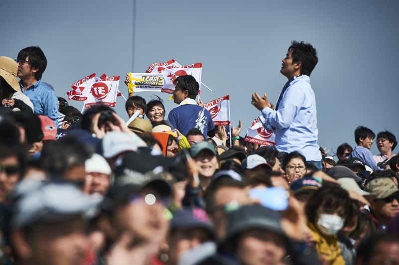 Spectators train their sights, for the first sign of the outcome for their compatriot Muroya.