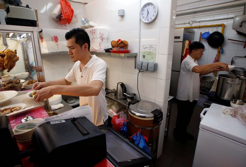 Hawker Derrick Lee, 30, and his mentor Zhu Yong Kun, 65, prepare chicken rice at their stall in a hawker centre in Singapore, June 30, 2016. — Reuters pic