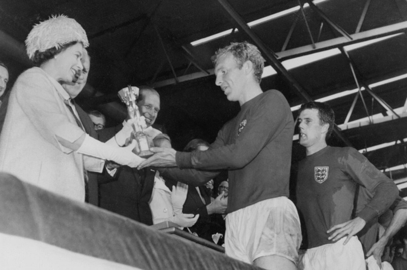 Queen Elizabeth presents the Jules Rimet Cup to Bobby Moore, captain of England's national team, as Prince Philip (centre) and forward Geoff Hurst (right) look on after England beat West Germany 4-2 in extra time in the World Cup final 30 July 1966 at Wem