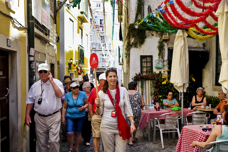 A tour guide leads a group of tourists through the streets of Alfama neighbourhood as locals sit at a terrace in Lisbon July 2, 2016. u00e2u20acu201d AFP pic