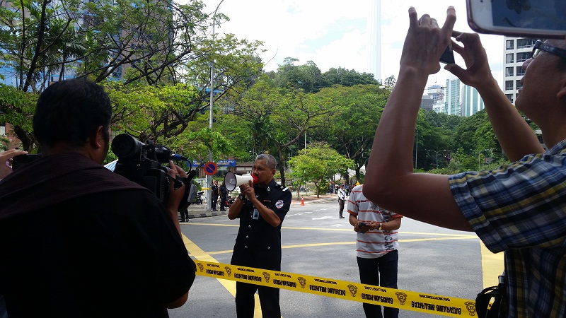 An auxiliary police officer informs those evacuated from the Bursa Malaysia building that it is safe for entry.― Picture by Ida Lim