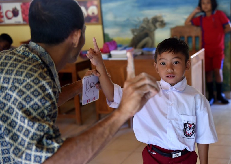 A teacher speaks with sign language to a deaf schoolboy during study at an elementary school at Bengkala village in Singaraja regency, Bali, July 20, 2016. — AFP pic