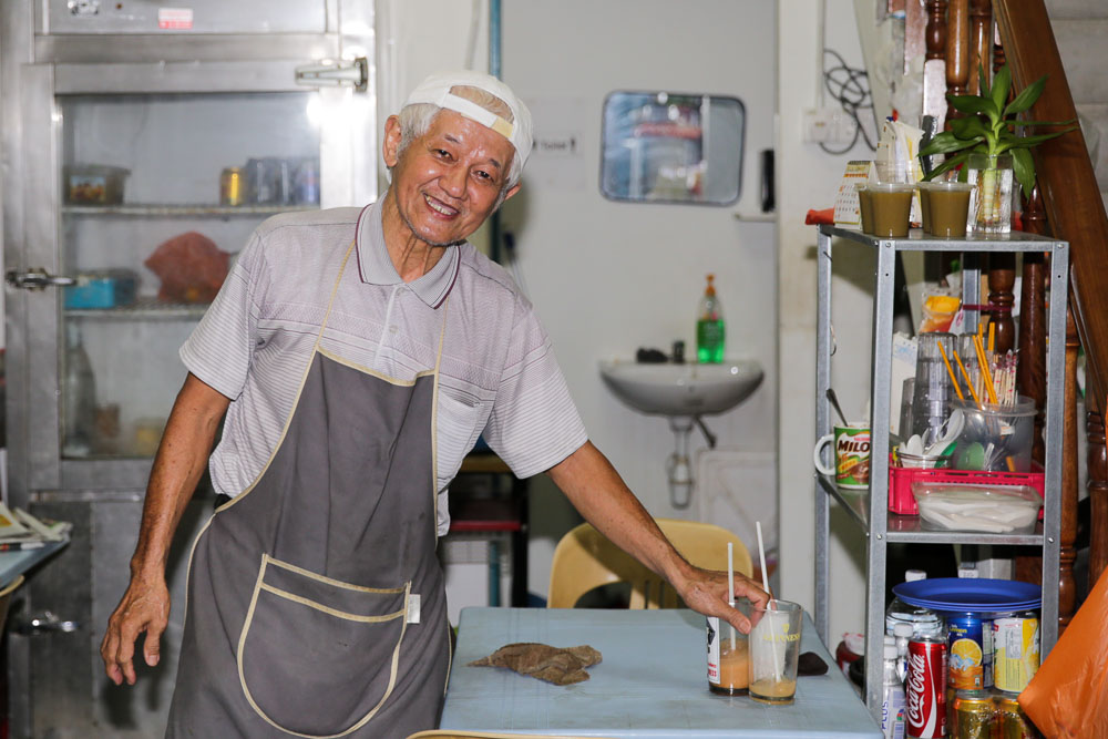 Uncle Lee smiling and posing inside his tiny Onn Loke Kopitiam.