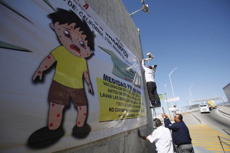 A worker (top) places a banner for a measles prevention programme during an awareness campaign by health workers at the Ciudad Juarez Mexican border crossing with El Paso, Texas February 16, 2015. u00e2u20acu201d Reuters pic