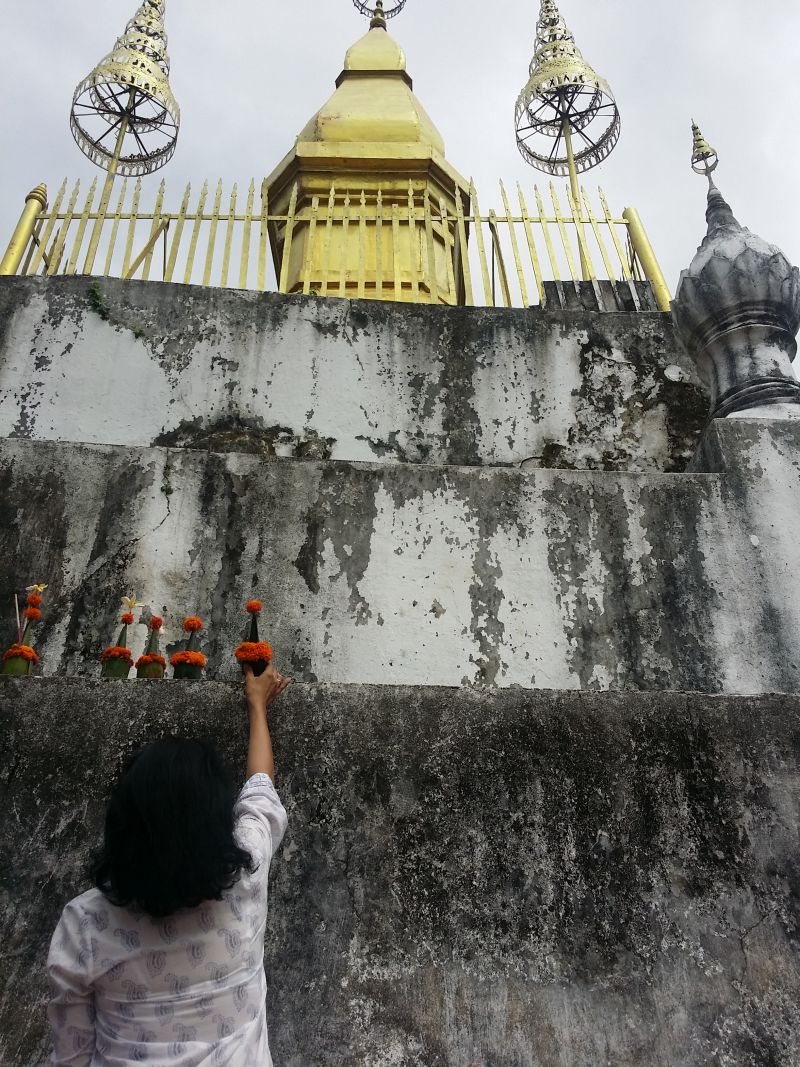 A woman placing offerings at Wat That Chomsi which was built in 1804.