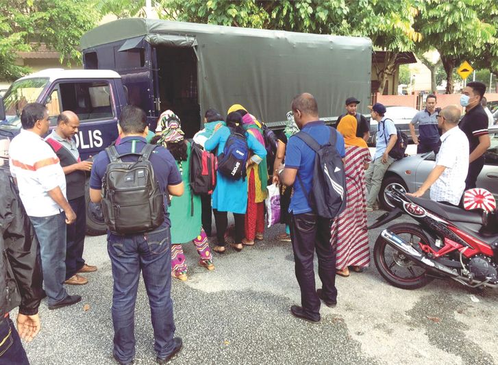 Police accompany some of the women rescued from the vice syndicate as curious onlookers gather. u00e2u20acu201d Picture by Royal Malaysian Police