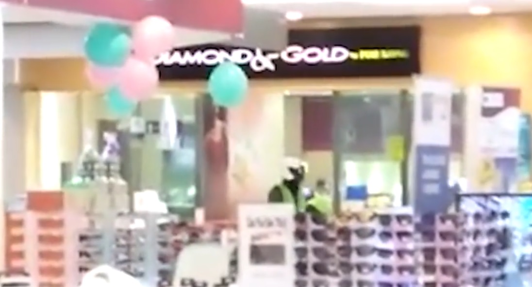 A video screenshot of the men moving about in the shop during the robbery, as an accomplice stands outside as a lookout. 