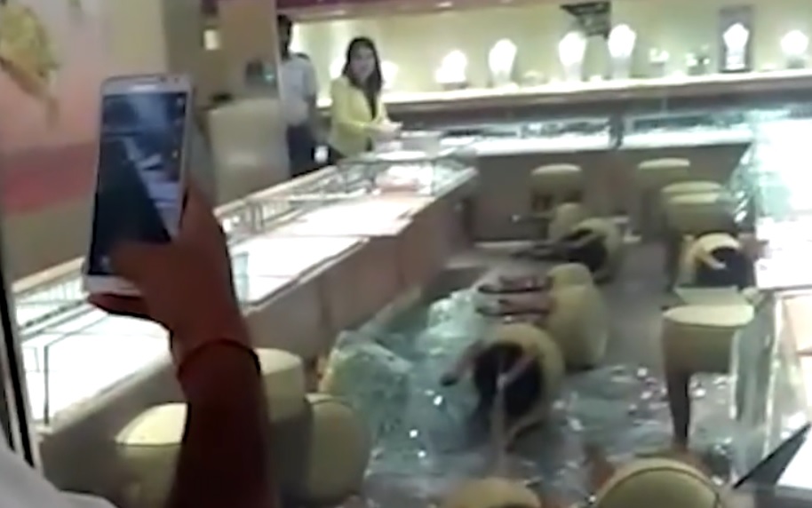 An employee attempting to arrange her smashed display, as the security guard stands behind her. 