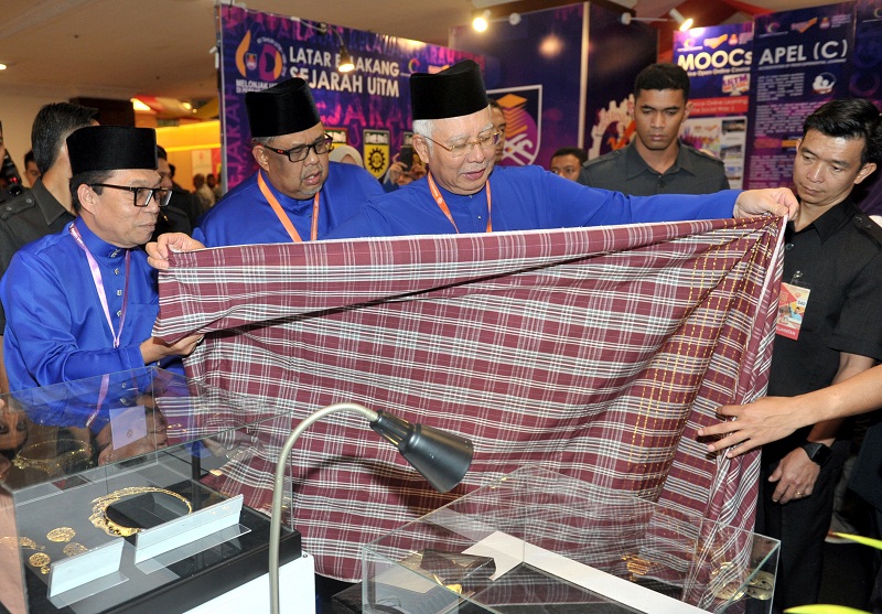 Presiden Umno Datuk Seri Najib Razak melihat sampin Kain Tenun Pahang corak Tun Razak yang dihadiahkan kepadanya oleh Pengarah Bahagian Creative Media dan Hub Teknologi Universiti Teknologi Mara (UiTM), Prof Madya Sulaiman Abdul Ghani (kiri) pada Perhimpu