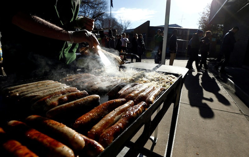 A grill covered in 'democracy sausages' is prepared alongside a line of voters queuing up at a polling station at Mount Alexander College in Flemington, Melbourne, July 2, 2016 on Australia's federal election day. u00e2u20acu201d Reuters pic