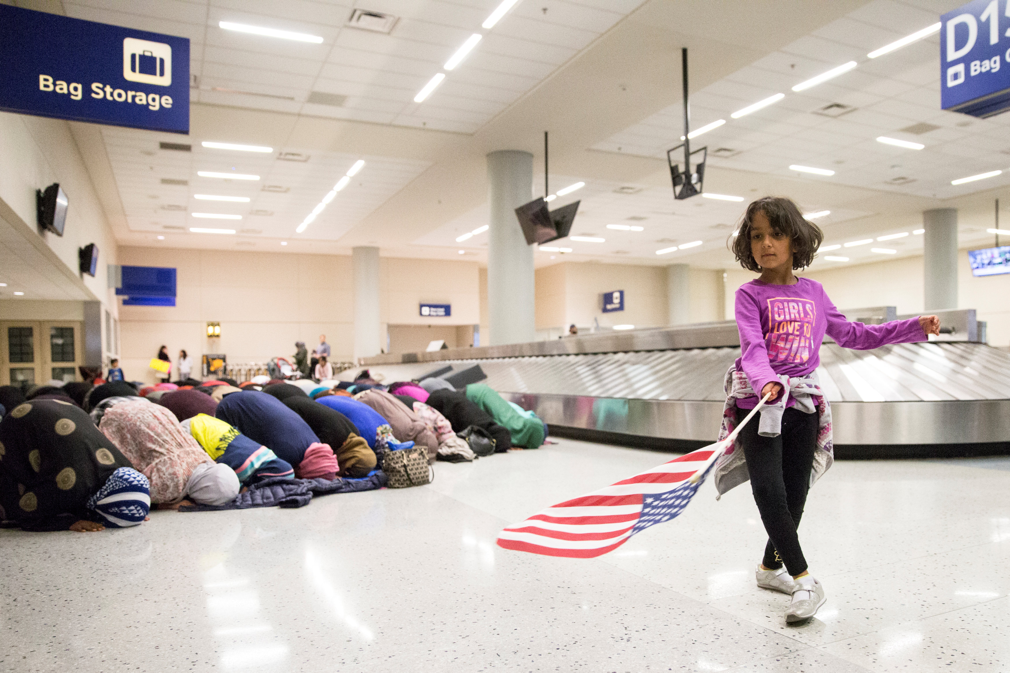 A young girl dances with an American flag in baggage claim while women pray behind her during a protest against the travel ban imposed by U.S. President Donald Trump's executive order, at Dallas/Fort Worth International Airport in Dallas, Texas, U.S. Janu