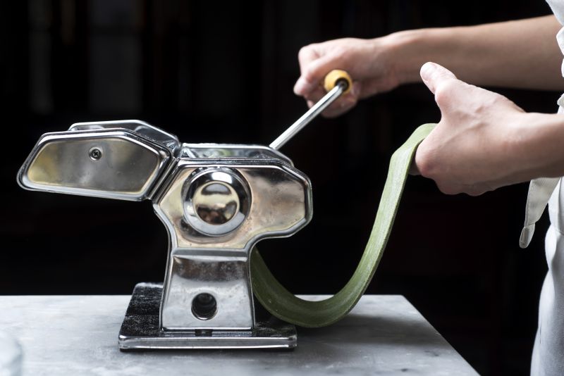 A pasta rolling machine is used to make a sheet of spinach pasta ― the device also has a cutting attachment for creating the noodles.