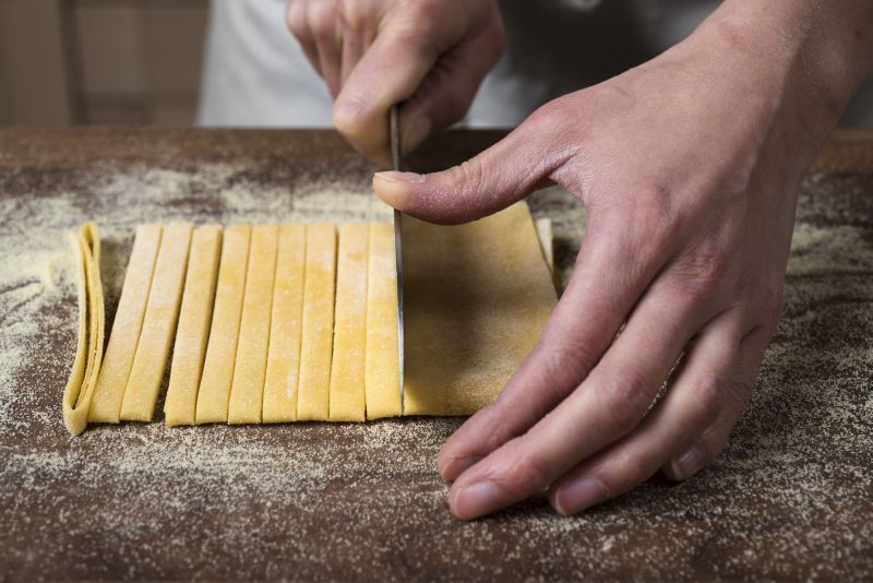 After folding rolled pasta dough into several layers, a knife is used to cut 1/4-inch-wide noodles from basic pasta dough.