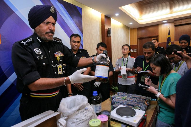 Kuala Lumpur police chief Datuk Amar Singh (left) showing a glass jar containing a liquid chemical believed to be used for drug processing, during a press conference on the seizure of drugs and firearms, at police headquarters in Kuala Lumpur May 22, 2017