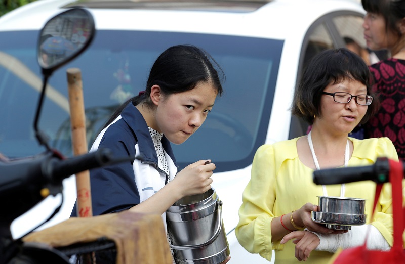 A student eats dinner brought in by her mother next to the entrance of Maotanchang Middle School, in Maotanchang town of Luan, Anhui province, China June 2, 2017.