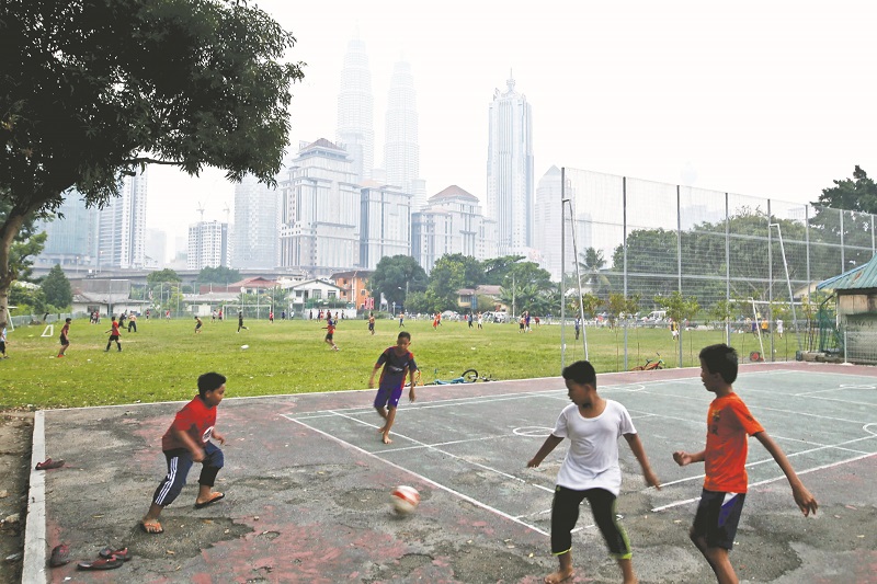 Local residents play football in Kampung Baru against the backdrop of KL city skyline and the iconic Petronas Twin Towers.