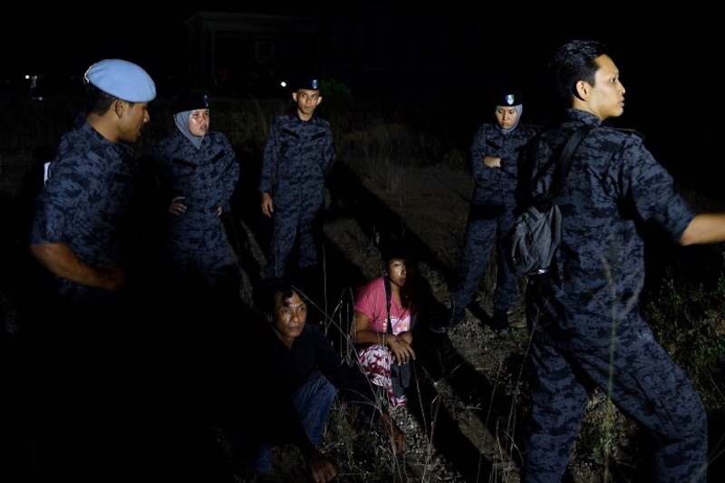 Migrant workers sit amidst Malaysian immigration officials in an open field following a raid at a construction site in Port Dickson July 11, 2017. u00e2u20acu201d AFP pic