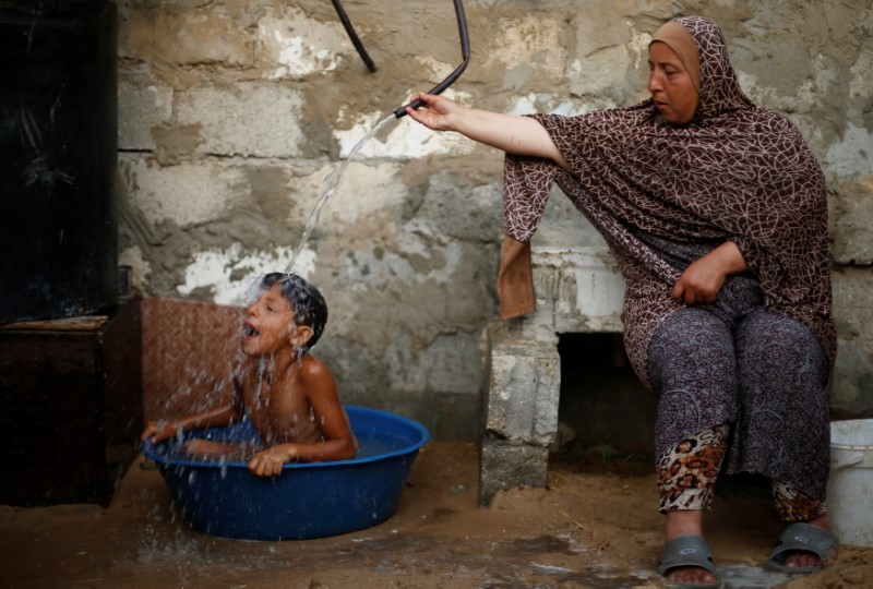 A Palestinian woman bathes her son with water from a tank, filled by a charity, inside their dwelling in Khan Younis, in the southern Gaza Strip, July 3, 2017. u00e2u20acu201d Reuters pic