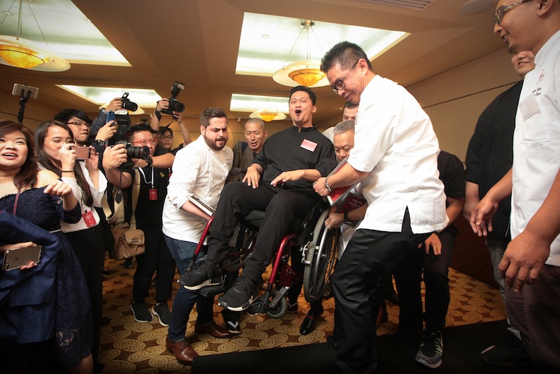 Chef Haikal Johari reacts as he is helped by other one-star Michelin recipients on stage for a group photo at the Michelin Guide Singapore 2017 Star Event on June 29, 2017. — TODAY pic